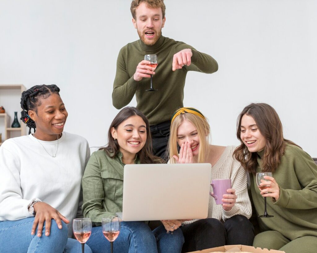 The picture shows a group of friends drinking while having a video call using a laptop. 